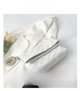 Detail of white quilted crossbody bag with chunky chain strap and textured finish