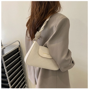 Close-up of cream textured baguette bag featuring woven shoulder strap and metal ring detail