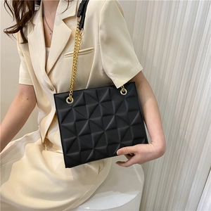 Black quilted tote bag with gold chain strap shown on a model for a modern minimalist look