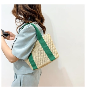 Detail of hand-woven straw tote bag with vibrant green canvas handles for summer