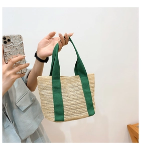 Close-up of hand-held woven straw tote bag with green canvas handles in a casual setting