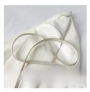 Detail of a creamy white leather shoulder strap with a silver metal hook on white fabric