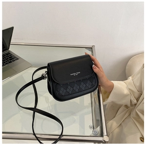 Detail of black crossbody bag with quilted texture and fashion trend logo on a desk