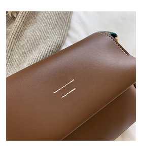Détail du sac bandoulière en cuir marron foncé avec coutures blanches minimalistes