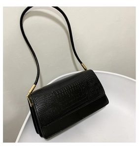 Detail of black crocodile pattern baguette bag featuring gold buckle and leather strap