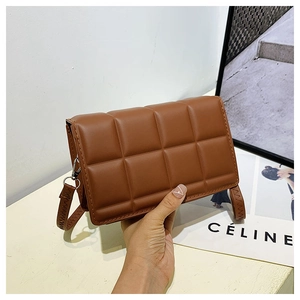 Detail of a brown quilted leather crossbody bag featuring 3D padded square pattern texture