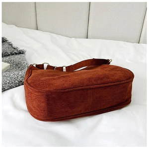Detail of brown suede shoulder bag with golden ring hardware in a cozy indoor setting