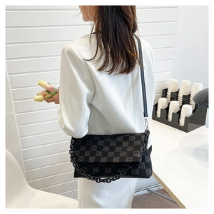 Detail of checkered chain bag with pleated texture and adjustable strap on a shoulder