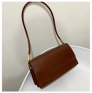 Detail of dark brown faux leather baguette bag showing crocodile pattern texture and gold hardware