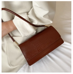 Close-up of brown crocodile pattern shoulder bag with polished gold metal hardware details
