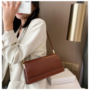Brown crocodile pattern baguette bag worn by model in a chic indoor setting