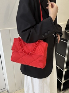 Sac à bandoulière matelassé rouge avec grosse chaîne porté par un mannequin en veste