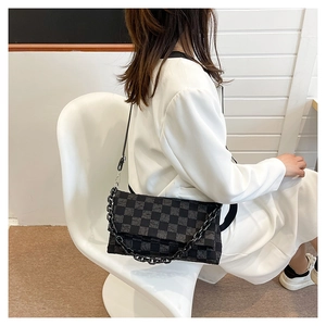 Detail of a chic black and grey checkered crossbody bag with chain strap on a model