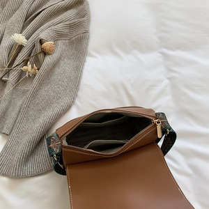 Sac bandoulière vintage marron avec sangle ethnique présenté sur une literie blanche