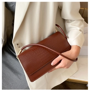 Close-up of brown crocodile pattern shoulder bag with golden hardware and white blazer
