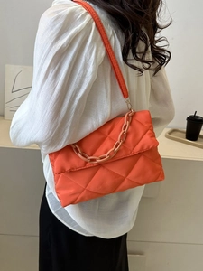 Détail d'un sac bandoulière matelassé orange vif avec chaîne en résine et texture en nylon