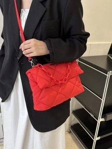 Détail d'un sac bandoulière rouge vif matelassé avec grosse chaîne décorative en plastique