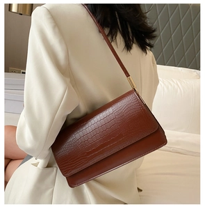 Brown crocodile pattern baguette bag worn over the shoulder with white blazer