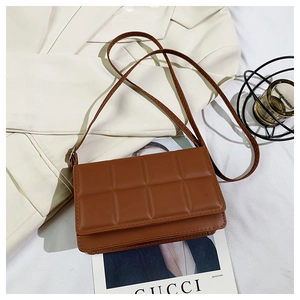 Detail of a dark coffee quilted faux leather crossbody bag on a white suit and magazine