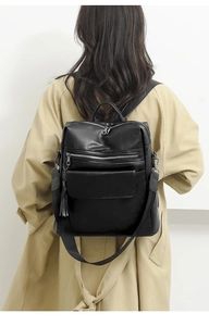 Close-up of black PU leather backpack with tassel detail on a khaki trench coat model