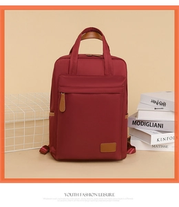 Detail view of burgundy waterproof nylon backpack with brown leather handles and zipper pulls