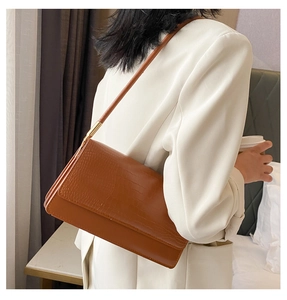 Detailed view of brown crocodile texture underarm bag with gold metal buckle accents