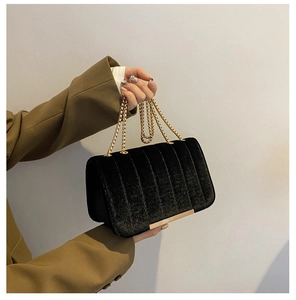 Detail of black velvet shoulder bag with vertical quilting and gold chain strap