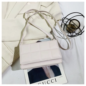 Detailed top view of light pink quilted crossbody bag on a white blazer and magazine