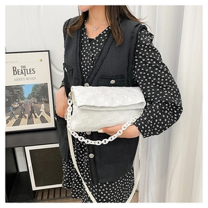 Detail of white quilted crossbody bag with chunky acrylic chain and leather strap on model