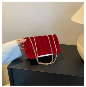 Close-up of elegant dark red velvet shoulder bag with gold chain and vertical quilting