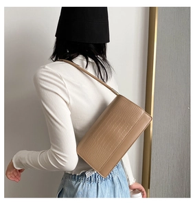 Close-up of khaki faux crocodile texture baguette bag worn by model over shoulder
