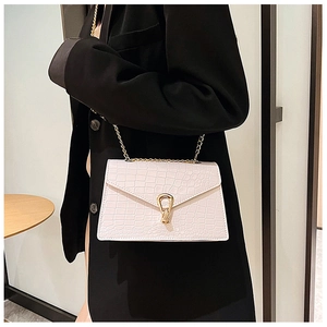 White crocodile embossed crossbody bag with gold chain strap worn over a black suit jacket