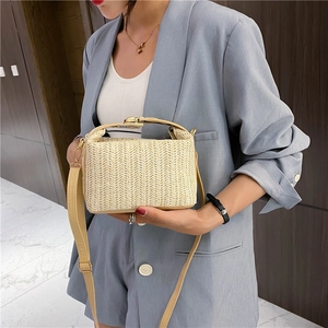 Elegante bolso tejido beige con correa de cuero y herrajes dorados en una modelo