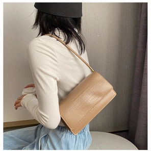 Detail of crocodile pattern texture and golden hardware on beige baguette shoulder bag