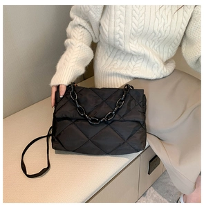Détail d'un sac bandoulière matelassé en nylon noir avec chaîne porté par un mannequin