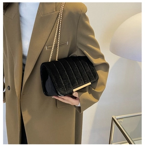 Close-up of black velvet shoulder bag with vertical quilting and gold chain strap