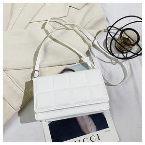 Close-up of a white quilted crossbody bag with adjustable strap on a beige blazer