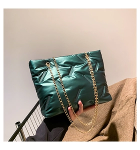 Detail of dark green quilted chain tote bag with metallic finish and padded texture