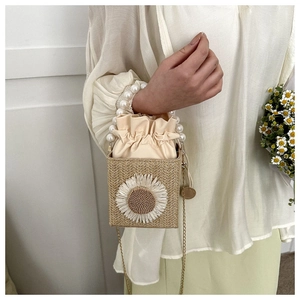 Detail view of woven straw box bag with large daisy embroidery and pearl top handle
