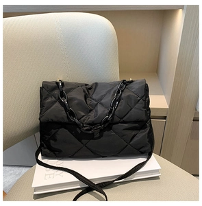 Détail du sac en nylon matelassé noir avec chaîne en résine sur un siège beige