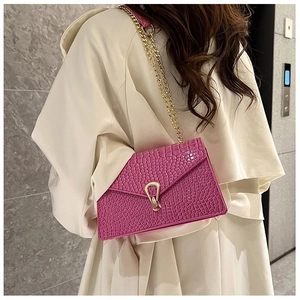 Close-up of rose red crocodile pattern crossbody bag with gold chain worn on shoulder