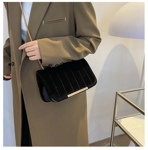 Detail of black velvet crossbody bag with gold chain strap on a brown coat