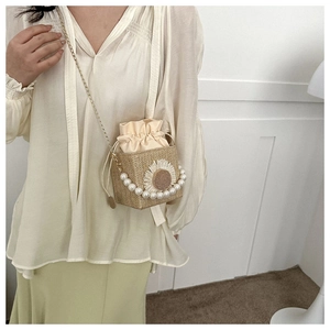 Detail of straw bucket bag with daisy embroidery, pearl handle, and gold metal chain strap