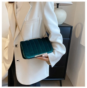 Close-up of dark green velvet handbag featuring vertical quilting and gold chain strap