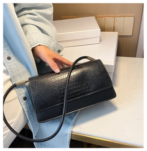 Detail of black crocodile pattern baguette bag featuring gold hardware and flap cover