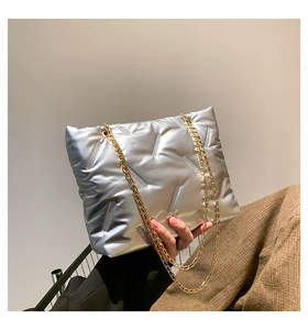 Detail of silver metallic quilted tote with dual gold chain straps held by a model