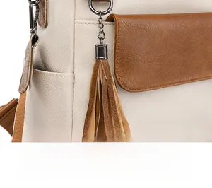 Detail of a dual-tone leather tassel charm on a beige PU backpack with metallic clip