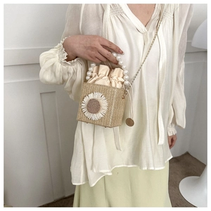 Detail of straw woven bucket bag with large sunflower ornament and pearl top handle