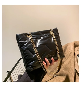 Detail of black quilted puffer tote bag featuring gold chain straps and V-pattern stitching