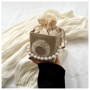 Detail of woven straw bucket bag with white daisy motifs and a large pearl handle